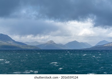 A rugged and wild coastline with mountains and stormy seas with whitecaps under and expressive cloudy sky