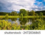 Ruhr River panorama near Schwerte Germany. Colorful evening atmosphere in springtime on the shore of calm reflecting water of a barrage. Sunlit idyllic scenery with trees after a may thunderstorm.