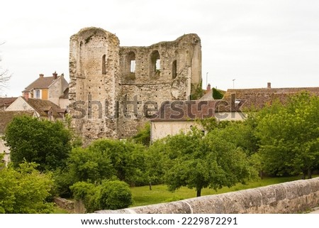 Ruined keep of a 12th century medieval stone castle in France. Tall trees with green leaves in early summer. Sky white with clouds and July light. Family holidays in Europe