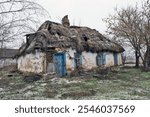 Ruined old clay house with thatched roof. Wooden windows, chimney. Ukrainian hut in abandoned village