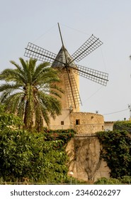 Ruined windmill on a ruined farm in the countryside in Spain in the fall. Classic Mallorca Island rural landscape an old mill and green palm tree. An old windmill in the countryside in the valley