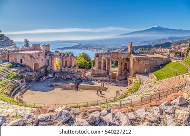 Ruinen des antiken griechischen Theaters in Taormina, Sizilien mit dem Doppelrauchschwanz des Ätna, der sich in der Morgensonne über die Bucht Giardini-Naxos des Ionischen Meeres erstreckt.