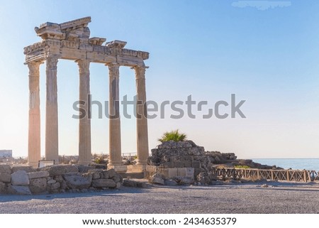 Ruins of Apollo's temple columns against sun, at sunrise, clear sky and calm sea in Side, Manavgat, Turkiye (Turkey).