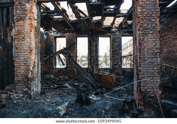 Ruins of burned brick house after fire disaster\
accident. Heaps of ash and arson, burnt furniture, collapsed roof,\
broken windows