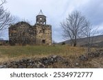 Ruins of the Church of St. Barbara (Barbare) of Sarkineti. Stone walls, collapsed bell tower dome. Trees without leaves, autumn grass. Cloudy sky in the background