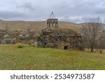 Ruins of the Church of St. Barbara (Barbare) of Sarkineti. Stone walls, collapsed bell tower dome. Trees without leaves, autumn grass. Cloudy sky and roofs of village houses in the background