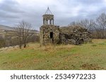 Ruins of the Church of St. Barbara in the village of Sarkineti. Stone walls, collapsed bell tower dome. Trees without leaves, autumn grass. Cloudy sky in the background