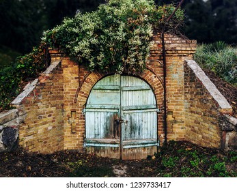 Ruins Of Old Cellar In Green Forest. Crawl Space With Lock On Shabby Blue Wooden Door. Concept - Entrance Denied.