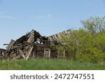 Ruins of a traditional village house. The old central residential architecture of Russia is destroyed and abandoned. Log cabin against a background of gray sky and green grass