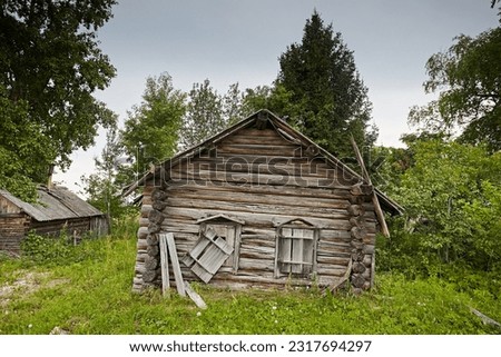 Ruins traditional village house. The old northern residential architecture of Russia is destroyed and abandoned. Log cabin on the background of gray sky and green grass