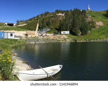 Ruka, Kuusamo /Finland - July 2018: Ski Lift Under Construction At Ruka Mountain Slalom Slope, Rowboat At Lake In Front Of Piste, Summer Flowers Blooming