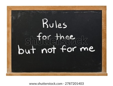 Rules for thee but not for me written in white chalk on a black chalkboard isolated in a wooden frame on white