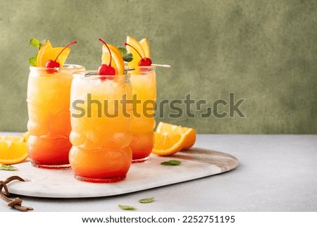 Rum punch in tiki glasses garnished with orange slices and a cherry with copy space