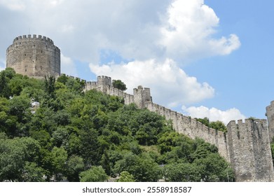 Rumeli Fortress, an ancient stone structure in Istanbul, Turkey, surrounded by lush greenery and standing against a bright blue sky with clouds - Powered by Shutterstock