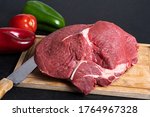 rump on a cutting board with a knife beside it with red pepper and green pepper in the background