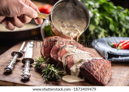 Rump steak cut to slices on a chopping board next to a knife and rosemary, with a mushroom sauce poured over it.