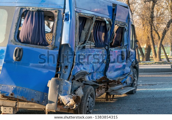 A rumpled\
blue minibus is on the road after an accident. Accident on the road\
in the city on a sunny day. A truck crashed into a minibus and\
crashed a car. Broken blue minivan close\
up