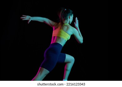 Run Away. Professional Runner, Jogger Running Isolated On Dark Background In Neon Light. Health, Sport, Fitness, Speed And Energy Concept. Athletic Woman In Sports Uniform And Footwear Training.