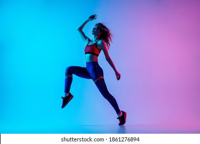 Run and jump. Young sportive woman training isolated on gradient blue-pink background in neon light. Athletic and graceful. Modern sport, action, motion, youth concept. Beautiful female practicing.