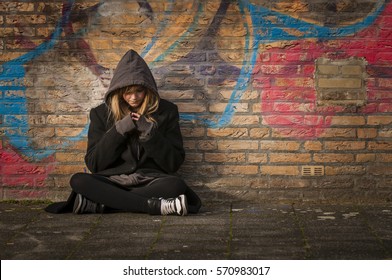 runaway girl thinks and sits in front of a wall with graffiti