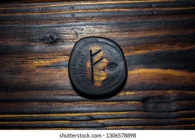 Rune Fehu carved from wood on a wooden background - Elder Futhark