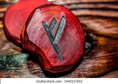 Rune Fehu red color carved from wood on a wooden background - Elder Futhark