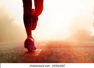 Runner athlete feet running on road. woman fitness silhouette sunrise jog workout wellness concept.