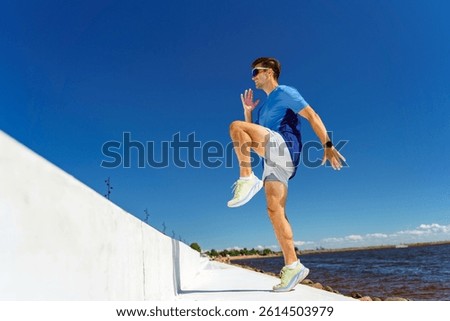 Runner Engaged in High Knee Exercise by the Waterfront Under a Bright Blue Sky Amidst a Serene Landscape