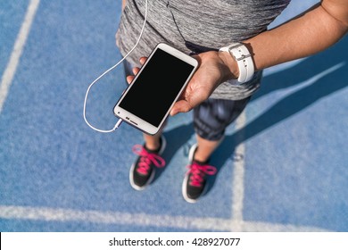 Runner girl holding smartphone using touchscreen for choosing music or texting sms on app before running on track. Female athlete woman feet and leg closeup with smartwatch and hand touching display.