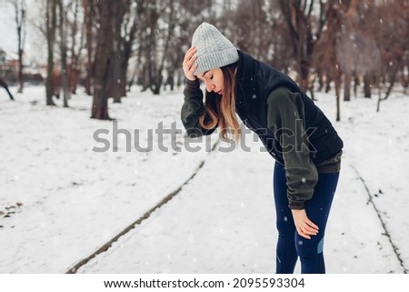 Runner having rest after training in snowy winter park. Woman working out outdoors during cold weather. Sportive lifestyle