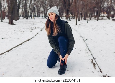 Runner Injured Leg During Training In Snowy Winter Park. Woman Feels Hurt, Ankle Pain. Dangerous Exercises Outdoors During Cold Weather