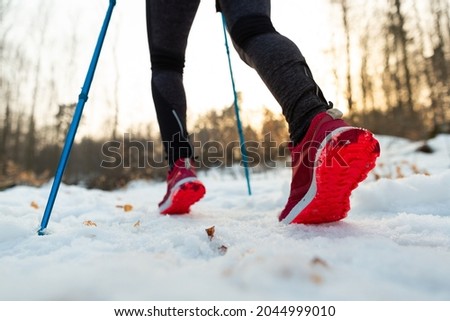 Runner Legs Running Up Snowy Mountain Trail in Winter. Cropped Bottom View of Female Tourist With Trekking Poles Walking Along Hiking Trail on Cold Winter Day.