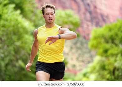 Runner looking at heart rate monitor smartwatch while running. Man jogging outside looking at his sports smart watch during workout training for marathon run. Fit male fitness model in his 20s. - Powered by Shutterstock