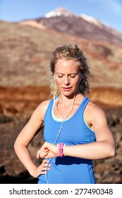 Runner Looking At Heart Rate Monitor Sports Smart Watch After Running With Earphones Listening To Music. Female Athlete Checking Pulse During Workout Run Exercise Outdoors In Beautiful Landscape.