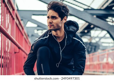 Runner man getting ready to run tying sneakers laces on bridge during listening audio records via electronic headphones, european jogger in sport tracksuit preparing for cardio exercises outdoors - Powered by Shutterstock