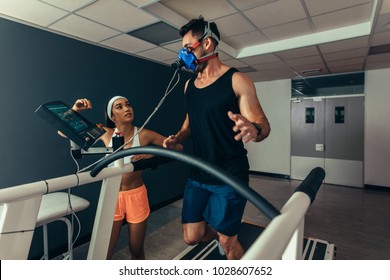 Runner with mask on treadmill in laboratory with woman standing by. Woman monitoring runner with mask on treadmill in laboratory - Powered by Shutterstock