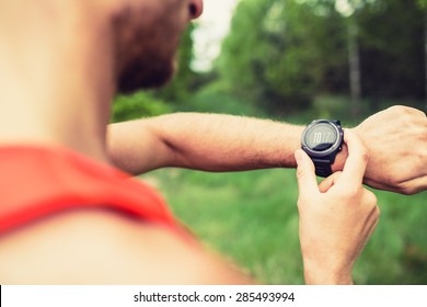 Runner on mountain forest trail checking looking at stopwatch smart watch, cross country runner checking performance, GPS position or heart rate pulse. Sport equipment in use outdoors on summer trail - Shutterstock ID 285493994
