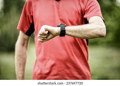 Runner on mountain trail looking at sportwatch smartwatch, checking performance on wearable monitor, gps navigation position map or heart rate pulse trace. Sport and fitness outdoors in nature.