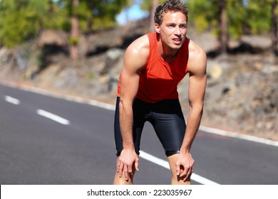 Runner resting after running. Jogging man taking a break during training outdoors in on mountain road. Young Caucasian male fitness model after work out.