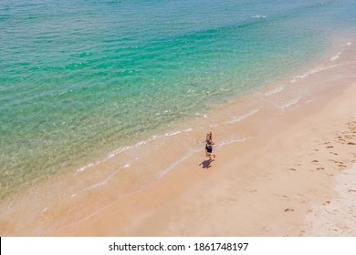 Runner Running On Beach By The Ocean - View From Above. Woman Athlete Training Cardio Jogging Doing Morning Workout. Hero Aerial Drone View Shot, Lots Of Copy Space