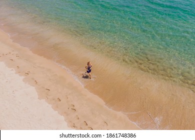 Runner Running On Beach By The Ocean - View From Above. Woman Athlete Training Cardio Jogging Doing Morning Workout. Hero Aerial Drone View Shot, Lots Of Copy Space