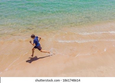 Runner Running On Beach By The Ocean - View From Above. Man Athlete Training Cardio Jogging Doing Morning Workout. Hero Aerial Drone View Shot, Lots Of Copy Space