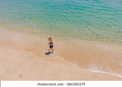 Runner Running On Beach By The Ocean - View From Above. Woman Athlete Training Cardio Jogging Doing Morning Workout. Hero Aerial Drone View Shot, Lots Of Copy Space