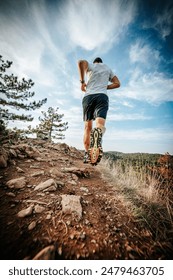 A runner running on a sunny trail under a blue sky.