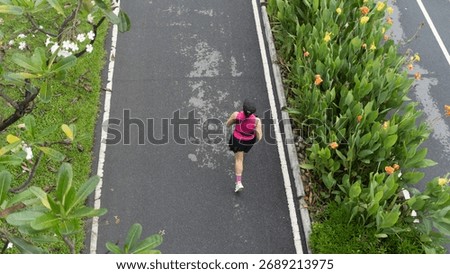A runner is seen from above as she moves along a paved path lined with greenery and flowers