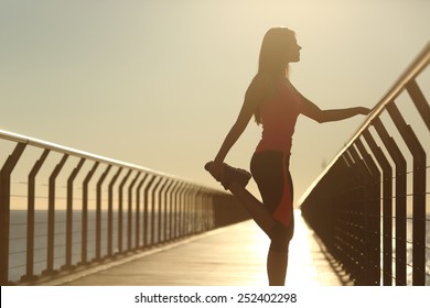 Runner silhouette doing stretching exercises at sunset in a bridge on the beach - Powered by Shutterstock