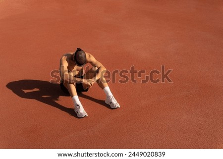 Runner sitting on the floor of a track crestfallen, disappointed by poor race results. Large copy space on the right. Sports loser concept