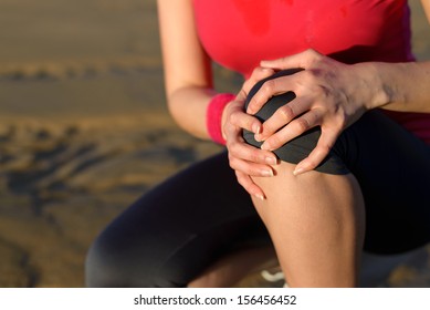 Runner sport knee injury. Woman in pain while running in beach. 
