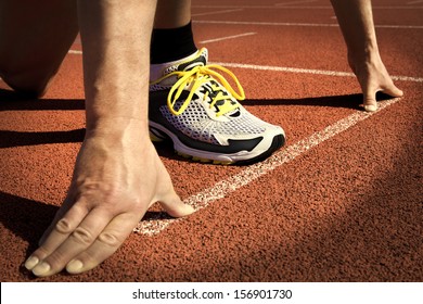 Runner In A Stadium Is In Start Position With Hands On The Line