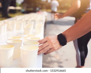 Runner Take Water During A Marathon Race. Marathon Runner Picking Up Water Cup At Service Point With Sunshine Morning. Selective Focus